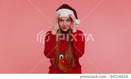 Woman in sweater Santa Christmas hat fooling around having closing eyes with hand and spying through Woman in sweater Santa Christmas hat fooling around having closing eyes with hand and spying through 84326819