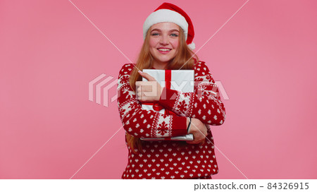 Cheerful girl in Christmas Santa sweater getting present gift box, expressing amazement happiness Cheerful girl in Christmas Santa sweater getting present gift box, expressing amazement happiness 84326915