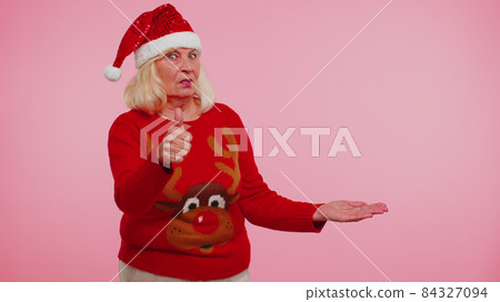 Grandmother in Christmas deer sweater showing thumbs up and pointing at on blank advertisement space Grandmother in Christmas deer sweater showing thumbs up and pointing at on blank advertisement space 84327094