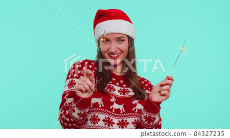 Lovely girl in Christmas Santa sweater dancing with bengal sparklers fireworks ligts, congratulation Lovely girl in Christmas Santa sweater dancing with bengal sparklers fireworks ligts, congratulation 84327235