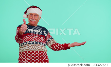 Grandfather in Christmas deer sweater showing thumbs up and pointing at on blank advertisement space Grandfather in Christmas deer sweater showing thumbs up and pointing at on blank advertisement space 84327835