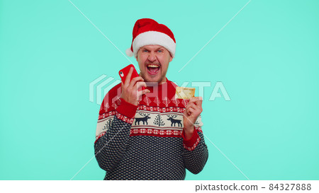 Man in Christmas red sweater use mobile cell phone and plastic credit bank card, win, calebrate, wow 84327888