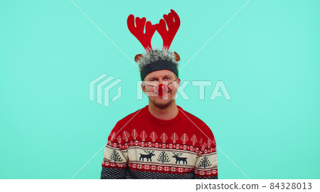 Cheerful lovely 30s years old man wears red New Year sweater and hat smiling, looking at camera Cheerful lovely 30s years old man wears red New Year sweater and hat smiling, looking at camera 84328013