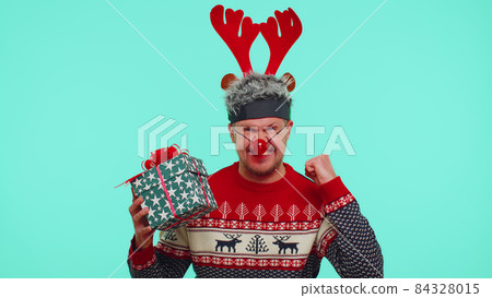 Man in Christmas sweater cries because not receive gift, after receiving present begins to rejoice Man in Christmas sweater cries because not receive gift, after receiving present begins to rejoice 84328015