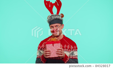 Cheerful man in sweater Santa Christmas hat getting present gift box, expressing amazement happiness Cheerful man in sweater Santa Christmas hat getting present gift box, expressing amazement happiness 84328017