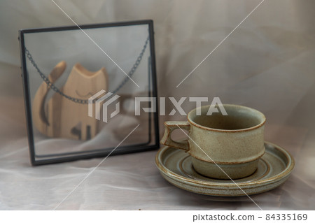 Handmade ceramic coffee mug with wooden doll in cat shape on fabric textured table cloth. 84335169