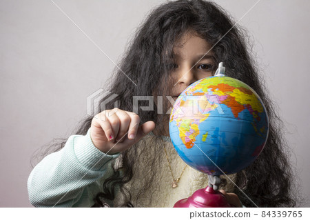 Little girl portrait holding a globe in hand and spin it by right hand 84339765