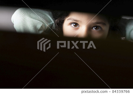 Little girl portrait behind black curtain looking in camera Little girl portrait behind black curtain looking in camera 84339766