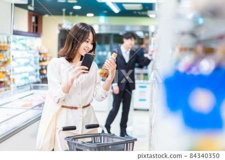 一位年輕女子在她的智能手機上查找超市產品 84340350