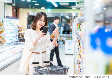 一位年輕女子在她的智能手機上查找超市產品 84340351