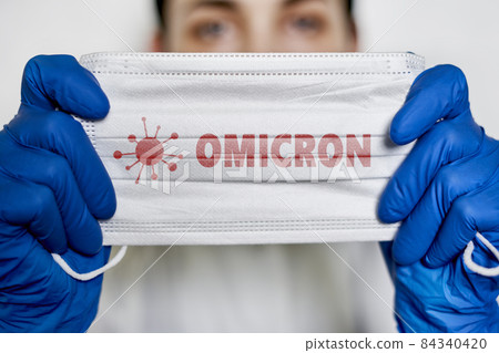 Female doctor holds a face mask with - Omicron variant text on it. Covid-19 new variant - Omicron. Omicron variant of coronavirus. SARS-CoV-2 variant of concern 84340420