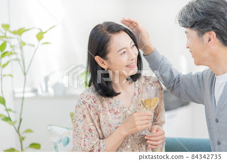 一個中年女人在客廳的沙發上喝酒，一個男人撫摸她的頭髮 84342735