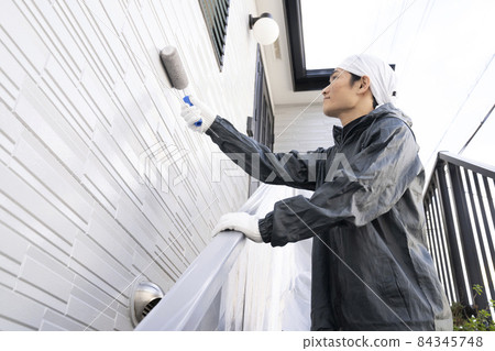 A painter who paints the exterior walls of a detached house with a roller 84345748