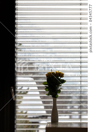 Dirty glass door. White ceramic vase with yellow rose on the table not in focus Dirty glass door. White ceramic vase with yellow rose on the table not in focus 84345777