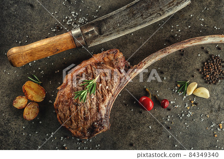 Grilled beef tomahawk steak fillet with ingredients and herbs on black board, product image for restaurant 84349340