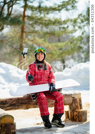 Woman with the snowboard using smartphone on a stick to making selfie Woman with the snowboard using smartphone on a stick to making selfie 84351306