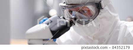 Scientist chemist in protective anti-plague suit looking through microscope in laboratory 84352179
