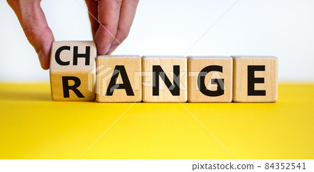 Change range symbol. Businessman turns a cube and changes the word 'change' to 'range'. Beautiful yellow table, white background. Copy space. Business and change range concept. 84352541