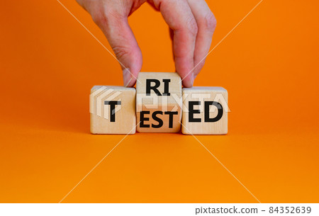 Tried and tested symbol. Businessman turns wooden cubes and changes the concept word 'tried' to 'tested' on a beautiful orange background. Copy space. Business and tried and tested concept. Tried and tested symbol. Businessman turns wooden cubes and changes the concept word 'tried' to 'tested' on a beautiful orange background. Copy space. Business and tried and tested concept. 84352639