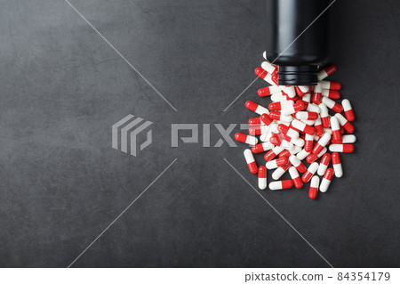 Red and white pills from a black jar on a black background. Red and white pills from a black jar on a black background. 84354179