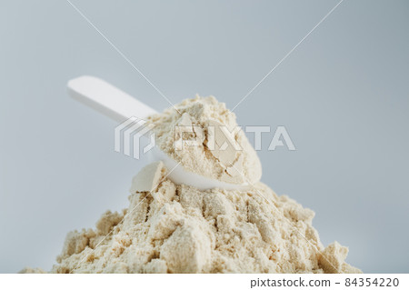 A pile of protein powder with a measuring spoon on a white background. 84354220