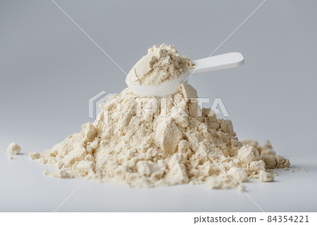 A mountain of soy protein isolate in powder with a measuring spoon on a white background. 84354221