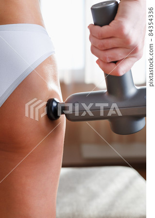 Self-massage of the female buttock with a percussion massage gun at home. 84354336