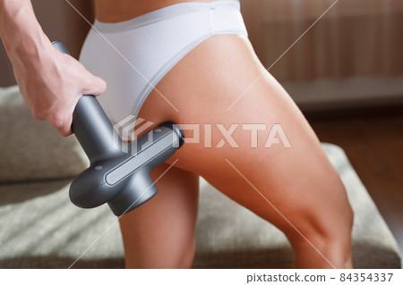 Self-massage of the female buttock with a percussion massage gun at home. Self-massage of the female buttock with a percussion massage gun at home. 84354337