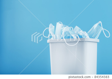 Waste bin full of used protective masks on a light blue background with free space. Waste bin full of used protective masks on a light blue background with free space. 84354383