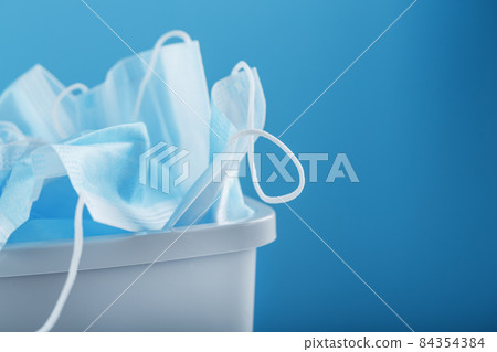 Waste bin full of used protective masks on a light blue background with free space. Waste bin full of used protective masks on a light blue background with free space. 84354384