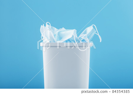 A white trash can full of virus protection masks on a blue background. 84354385