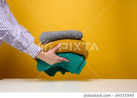 woman holding a stack of knitted folded sweaters on a yellow background. Washing clothes, cleaning things woman holding a stack of knitted folded sweaters on a yellow background. Washing clothes, cleaning things 84355849