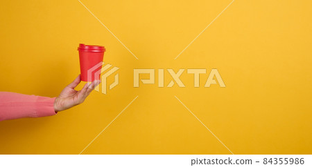 hand holds paper cardboard red cup for coffee, yellow background. Eco-friendly tableware, copy space hand holds paper cardboard red cup for coffee, yellow background. Eco-friendly tableware, copy space 84355986