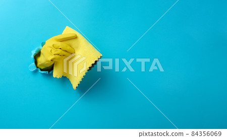 a hand in a yellow rubber cleaning glove holds a dry rag on a blue background. Part of the body stick out of the hole in the paper, banner a hand in a yellow rubber cleaning glove holds a dry rag on a blue background. Part of the body stick out of the hole in the paper, banner 84356069