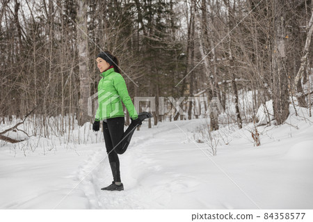 Runner in winter stretching out thighs and legs running in snow. Woman runner outside in winter in forest. Fit healthy sport lifestyle concept with young fitness model. Multiracial Asian Caucasian Runner in winter stretching out thighs and legs running in snow. Woman runner outside in winter in forest. Fit healthy sport lifestyle concept with young fitness model. Multiracial Asian Caucasian 84358577