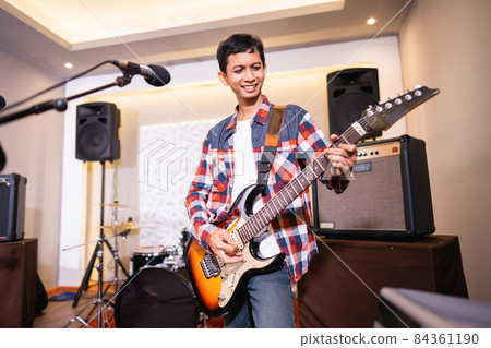 a male guitarist plays an electric guitar with a band in the background 84361190