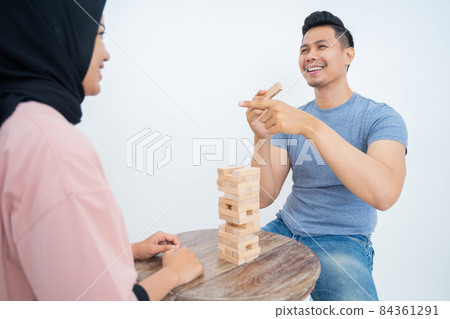Smiling man holding block with finger pointing at female friend Smiling man holding block with finger pointing at female friend 84361291