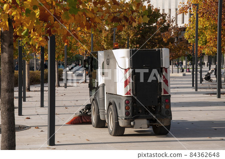 A swiper sweeps autumn leaves in a park square. 84362648