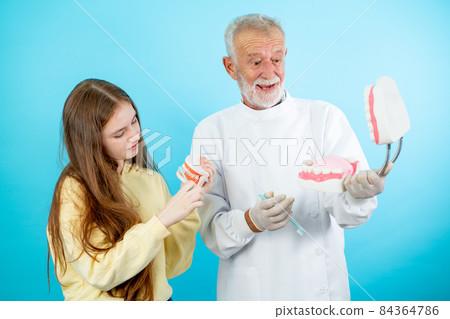 Senior dentist hold big model of teeth while young girl hold small one and they look fun action 84364786