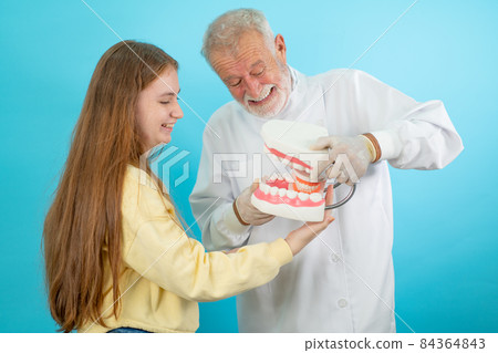 Senior dentist hold big model of teeth while young girl hold small one and they look fun action 84364843