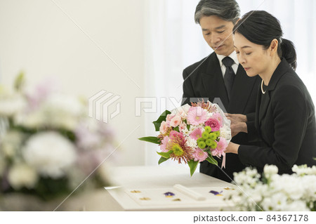 Middle-aged men and women offering bouquets to the casket 84367178