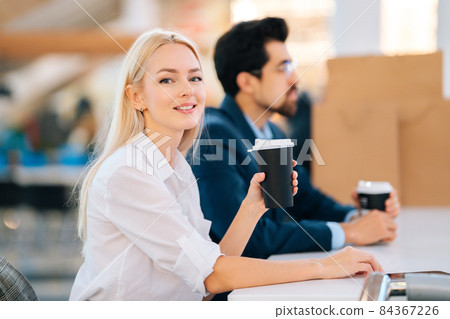 Beautiful young young man and woman drinking coffee and resting sitting at table in mall after shopping at mall, looking at camera. Beautiful young young man and woman drinking coffee and resting sitting at table in mall after shopping at mall, looking at camera. 84367226