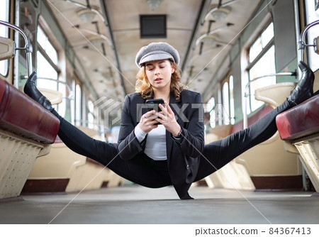 Flexible girl sitting on the split in underground carriage with smartphone. Concept of creativity, individuality and self confidence 84367413