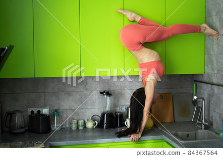 Woman on the kitchen doing exercise and handstand. Concept of individuality, creativity and self-confidence 84367564