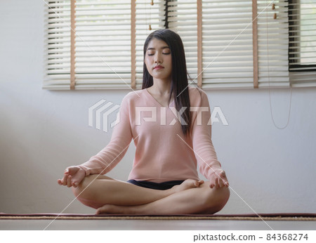 Morning yoga with an Asian woman, sitting in Easy position, Sukhasana posture, and meditating online. 84368274