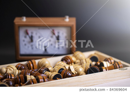 Chess pieces on a board and a chess clock on a dark background 84369604