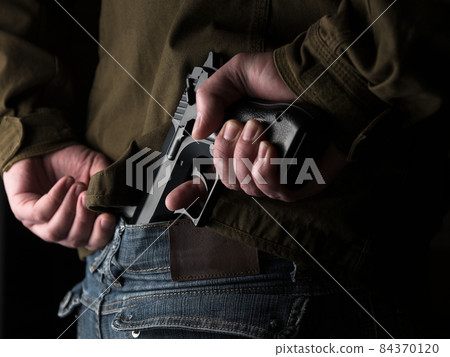 Man hiding a gun behind his back Man hiding a gun behind his back 84370120