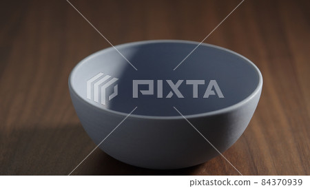 Blue ceramic bowl on walnut wood table closeup Blue ceramic bowl on walnut wood table closeup 84370939