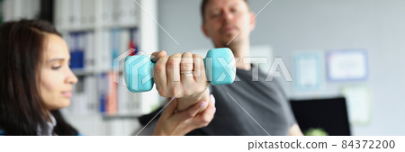 Rehabilitation therapist helping disabled man in wheelchair to lifting dumbbell in closeup Rehabilitation therapist helping disabled man in wheelchair to lifting dumbbell in closeup 84372200