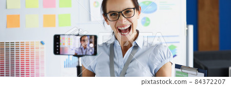 Young woman rejoicing and holding documents in front of mobile phone camera on tripod Young woman rejoicing and holding documents in front of mobile phone camera on tripod 84372207